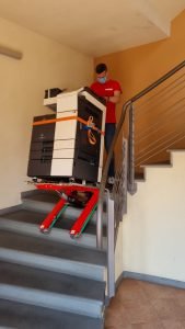 Un homme transporte la photocopieuse dans les escaliers avec le chariot d'escalier Domino