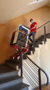 Un homme transporte la photocopieuse dans les escaliers avec le chariot d'escalier Domino