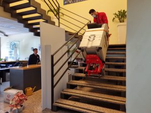 Un homme transporte la photocopieuse dans les escaliers avec le chariot d'escalier Domino