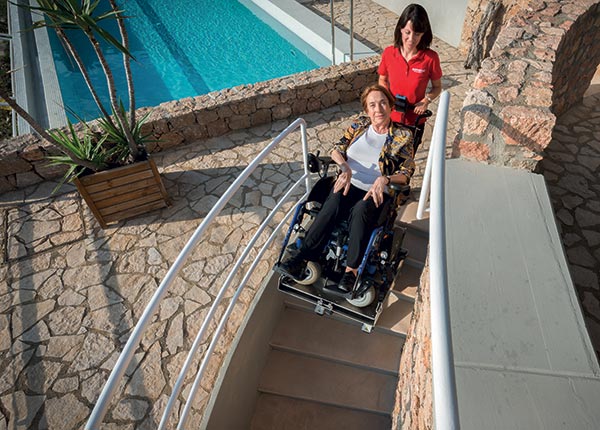 Transport d'une personne âgée et handicapée en fauteuil roulant dans les escaliers avec le monte-escalier électrique Domino People